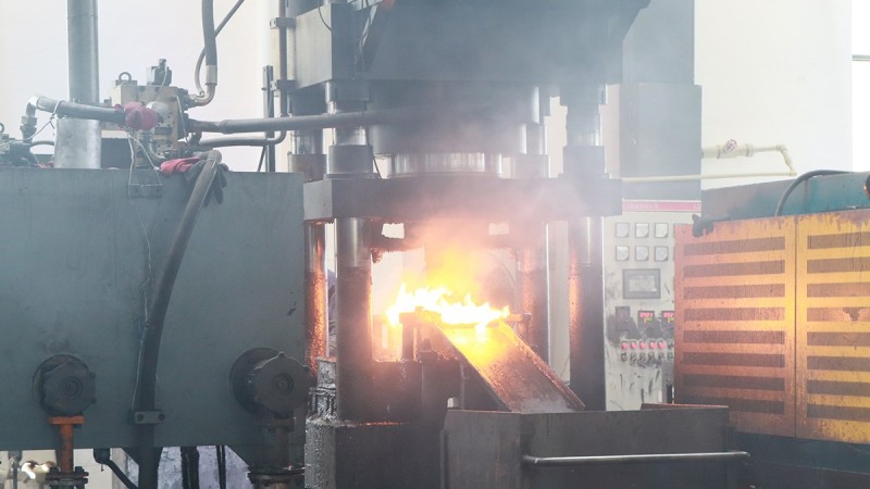 Heated aluminium billet entering a forging press during wheel spacer production